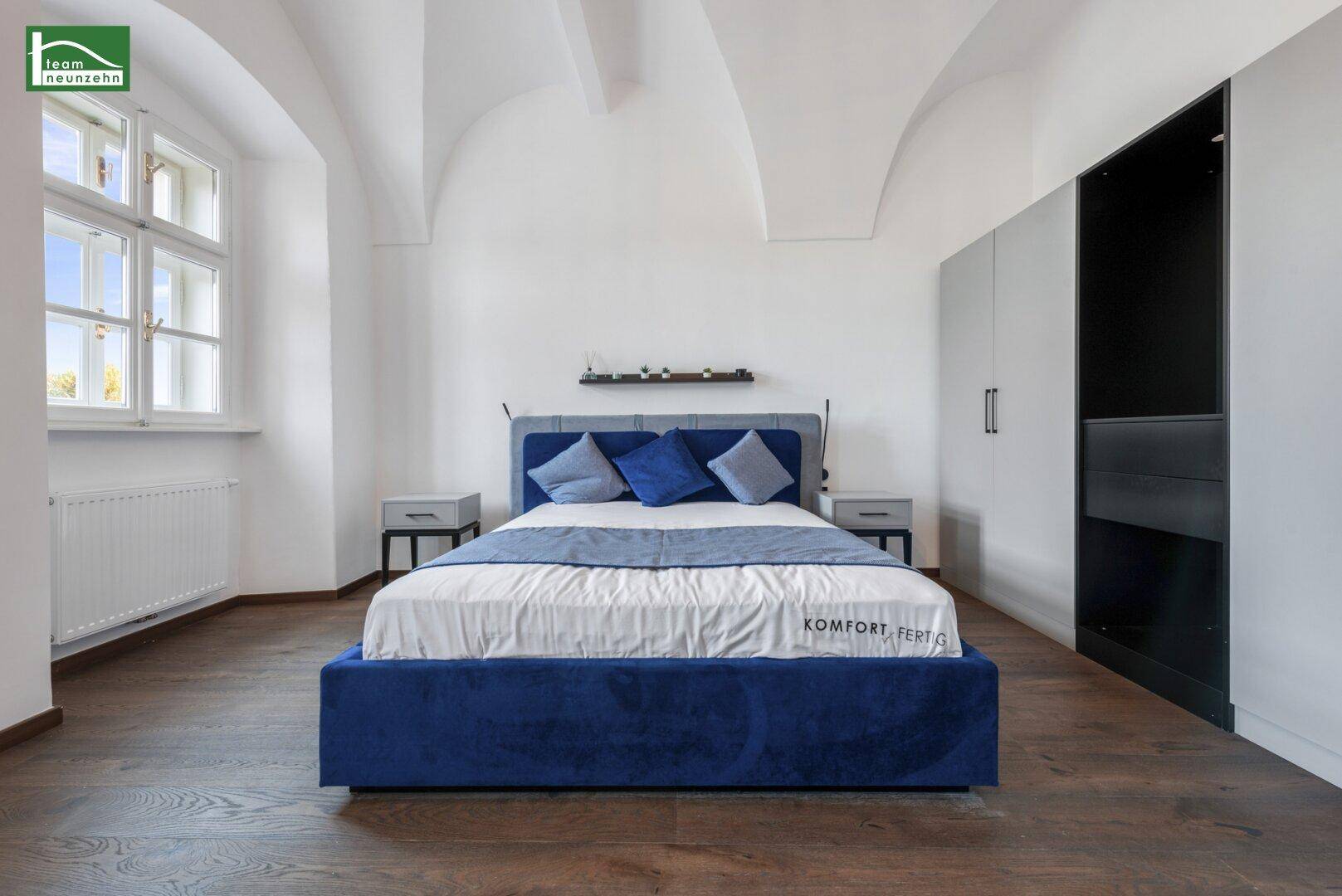 Geräumiges Schlafzimmer mit blauem Bett, Holzboden und Einbauschränken.