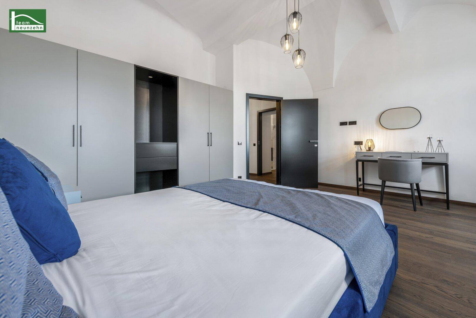 Schlafzimmer mit blauem Bett, Einbauschränken und Schreibtischbereich.