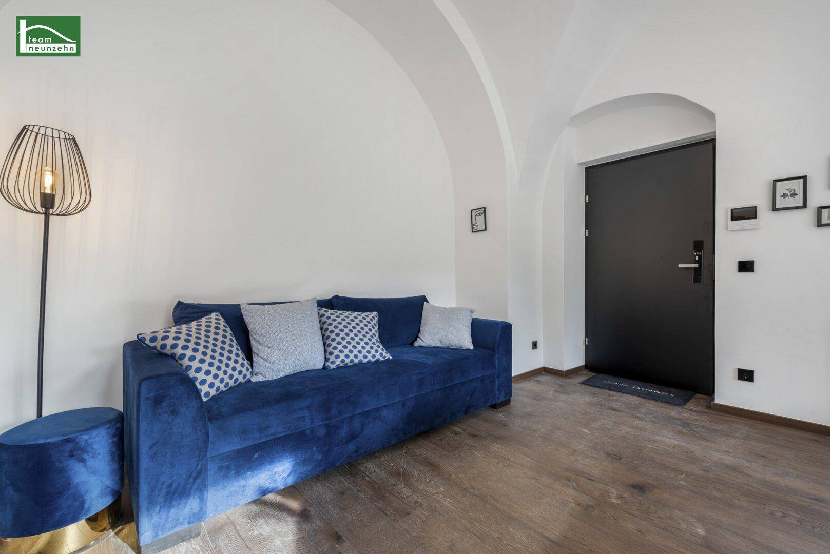 Gemütlicher Wohnbereich mit blauem Sofa, Holzboden und Gewölbedecke.