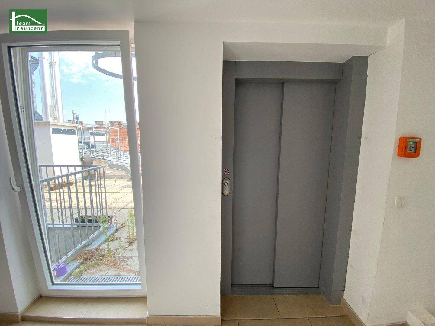 Heller Flur mit modernem Aufzug und Zugang zu einer Dachterrasse mit Rampe.