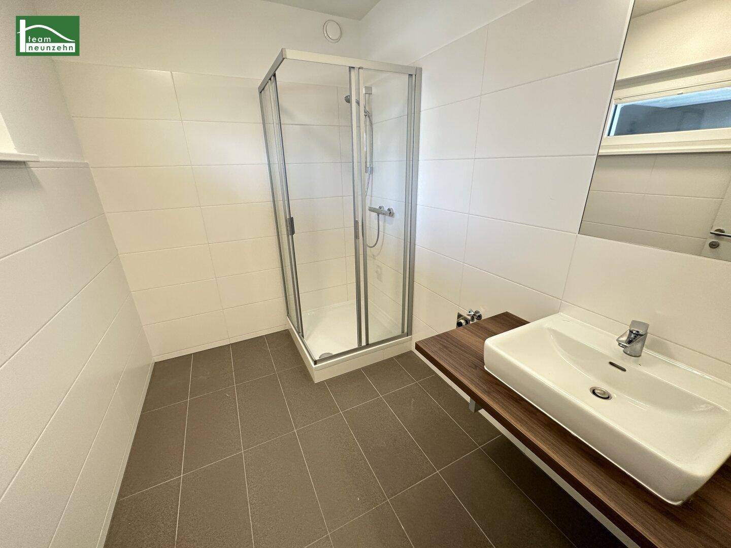 Modernes Badezimmer mit Duschkabine, Waschbecken und großen weißen Fliesen an den Wänden.