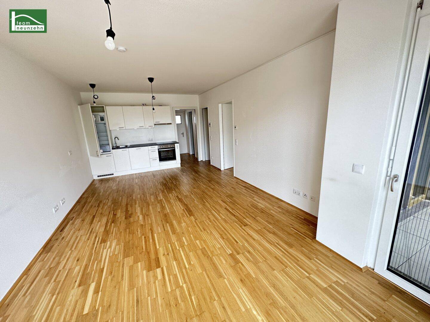 Offener Wohnbereich mit Holzboden und integrierter Küchenzeile, ideal für modernes Wohnen.