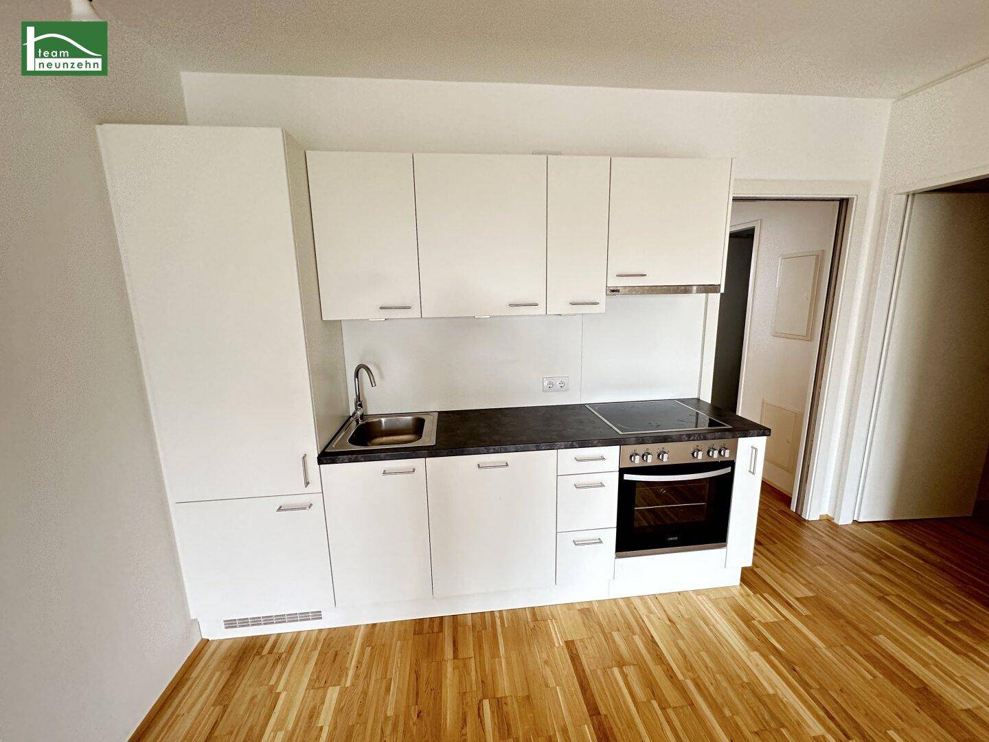 Kompakte, moderne Küchenzeile mit weißen Schränken, Spüle und Kochfeld in hellem Raum.