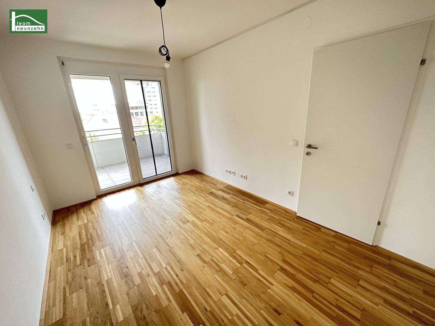 Helles, leeres Zimmer mit Parkettboden und Zugang zu einem Balkon, bereit zur Einrichtung.