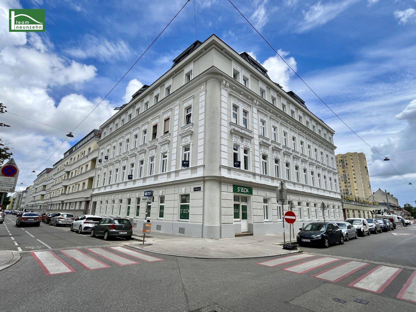 Das Eckgebäude an einer belebten Kreuzung mit klassischer Architektur und Geschäften im Erdgeschoss.