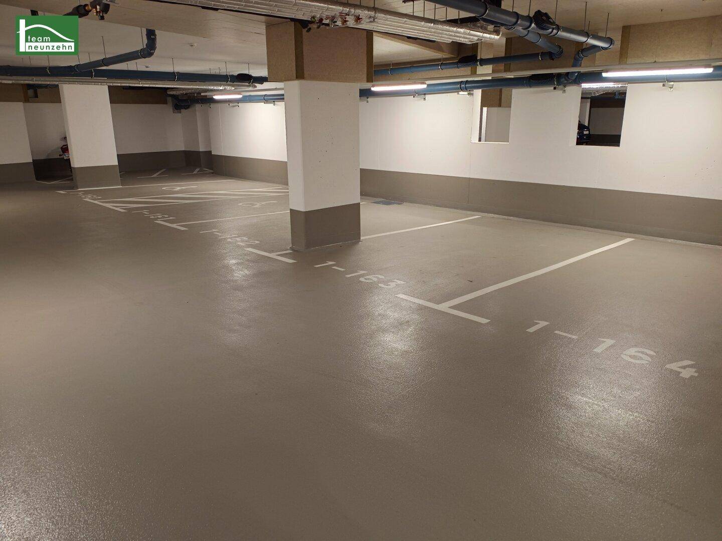 Tiefgarage mit markierten Stellplätzen, Betonsäulen und sichtbaren Installationen an der Decke.