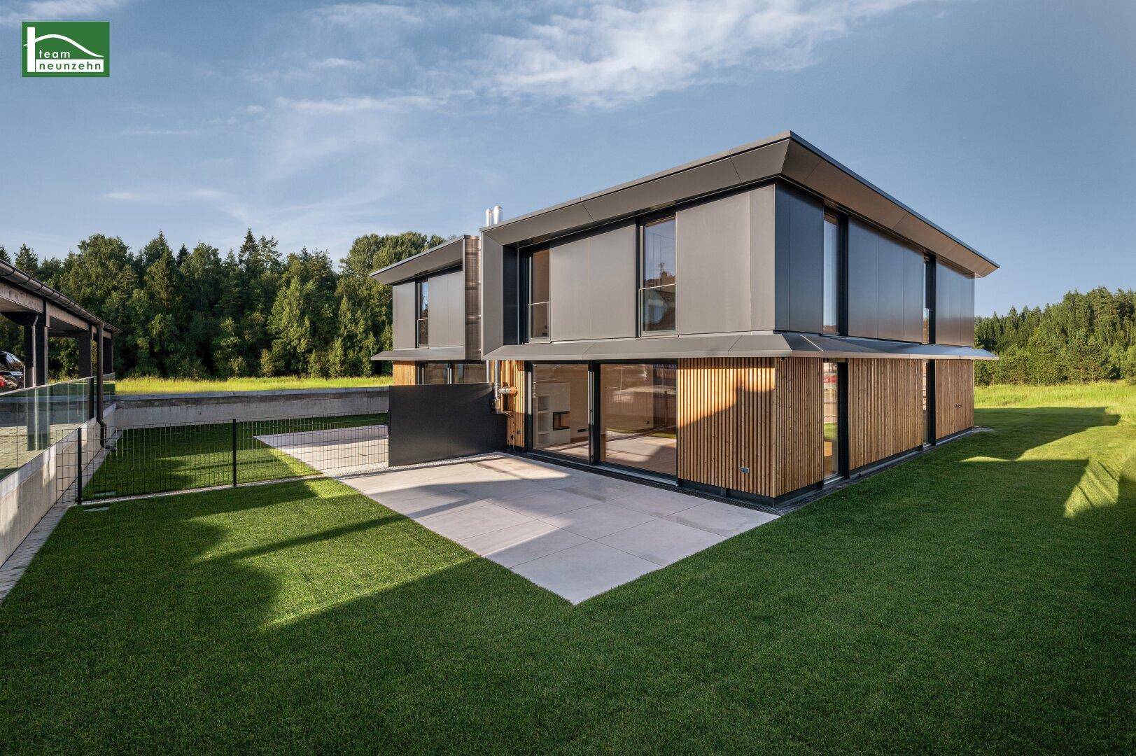 Modernes Haus mit Holzverkleidung, großen Glasfronten und einer sonnigen Terrasse im Grünen.
