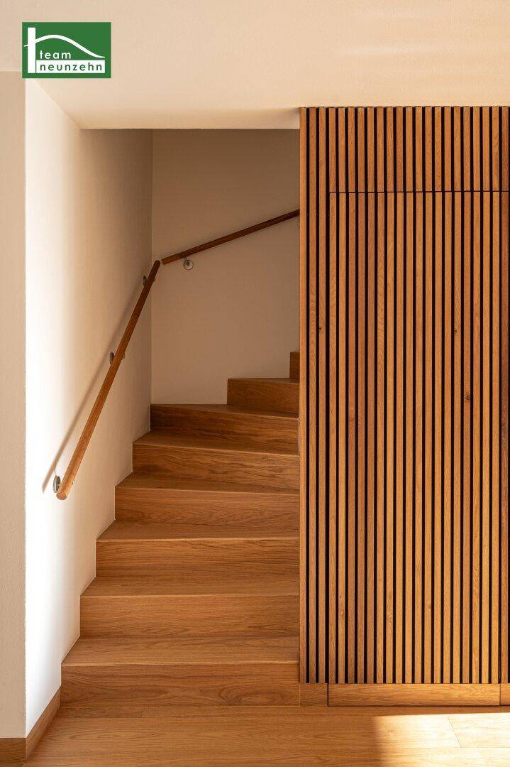 Elegante Holztreppe mit passendem Handlauf, umgeben von einer modernen Holzlamellenwand.