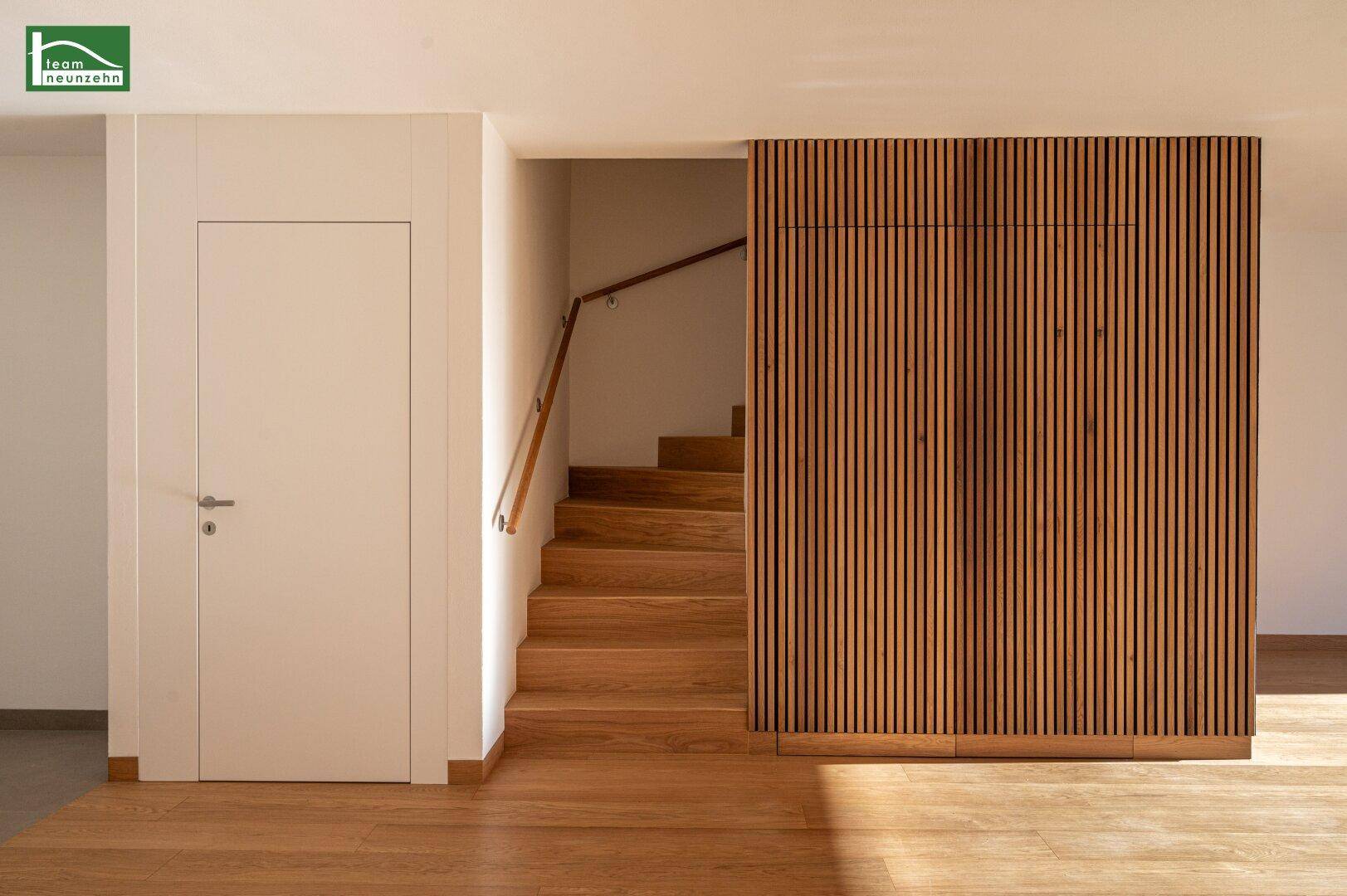 Heller Treppenaufgang mit Holzstufen und moderner Holzlamellenwand in einem Neubau.