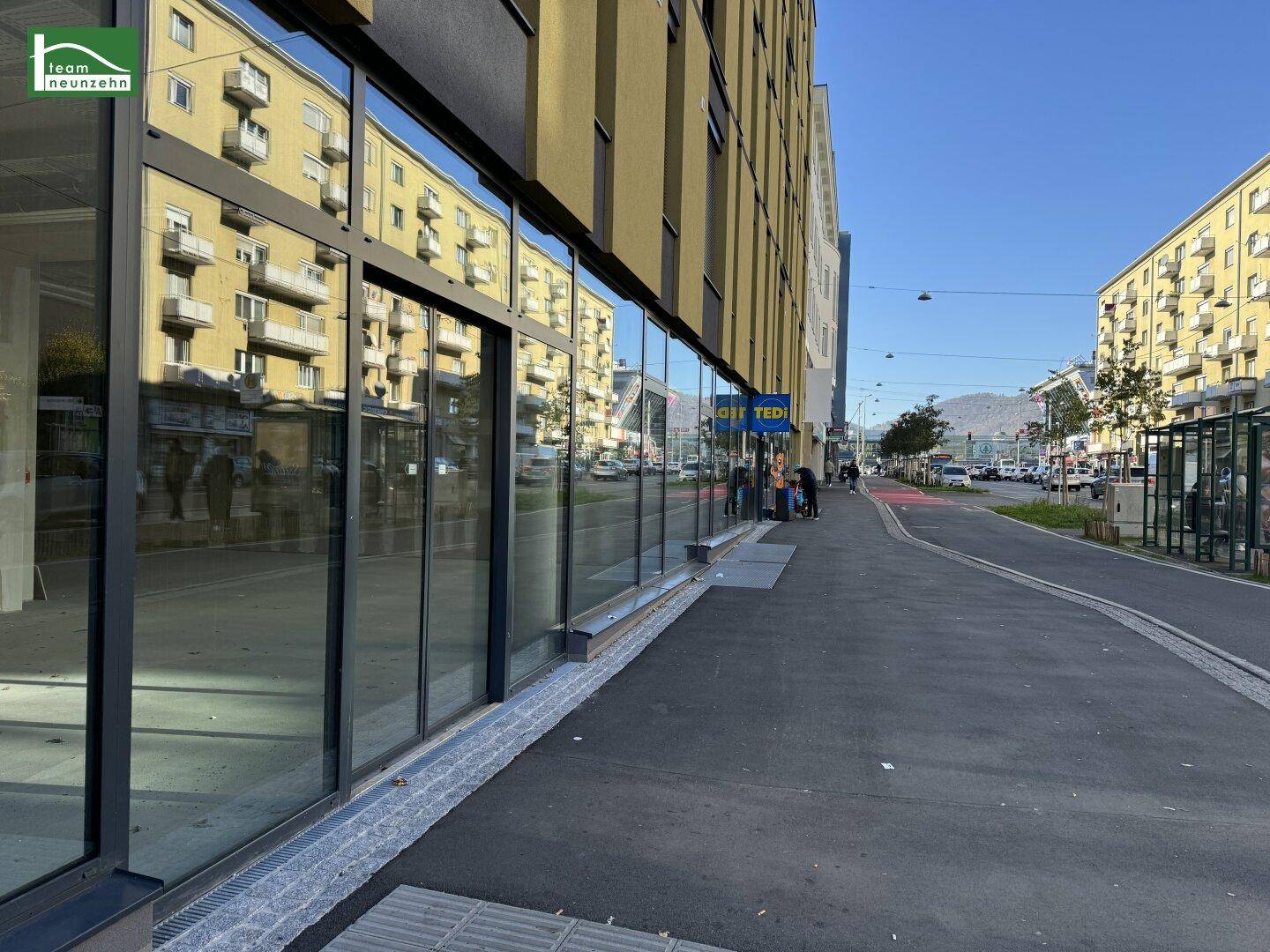Blick entlang der modernen Glasfassade des Geschäftsgebäudes mit Bürgersteig und Straße in der Stadt.