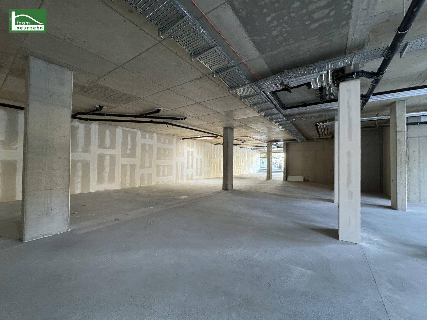 Unfertiger Gewerberaum mit Betonboden und -decke, sichtbaren Installationen und teilweise verputzten Wänden.