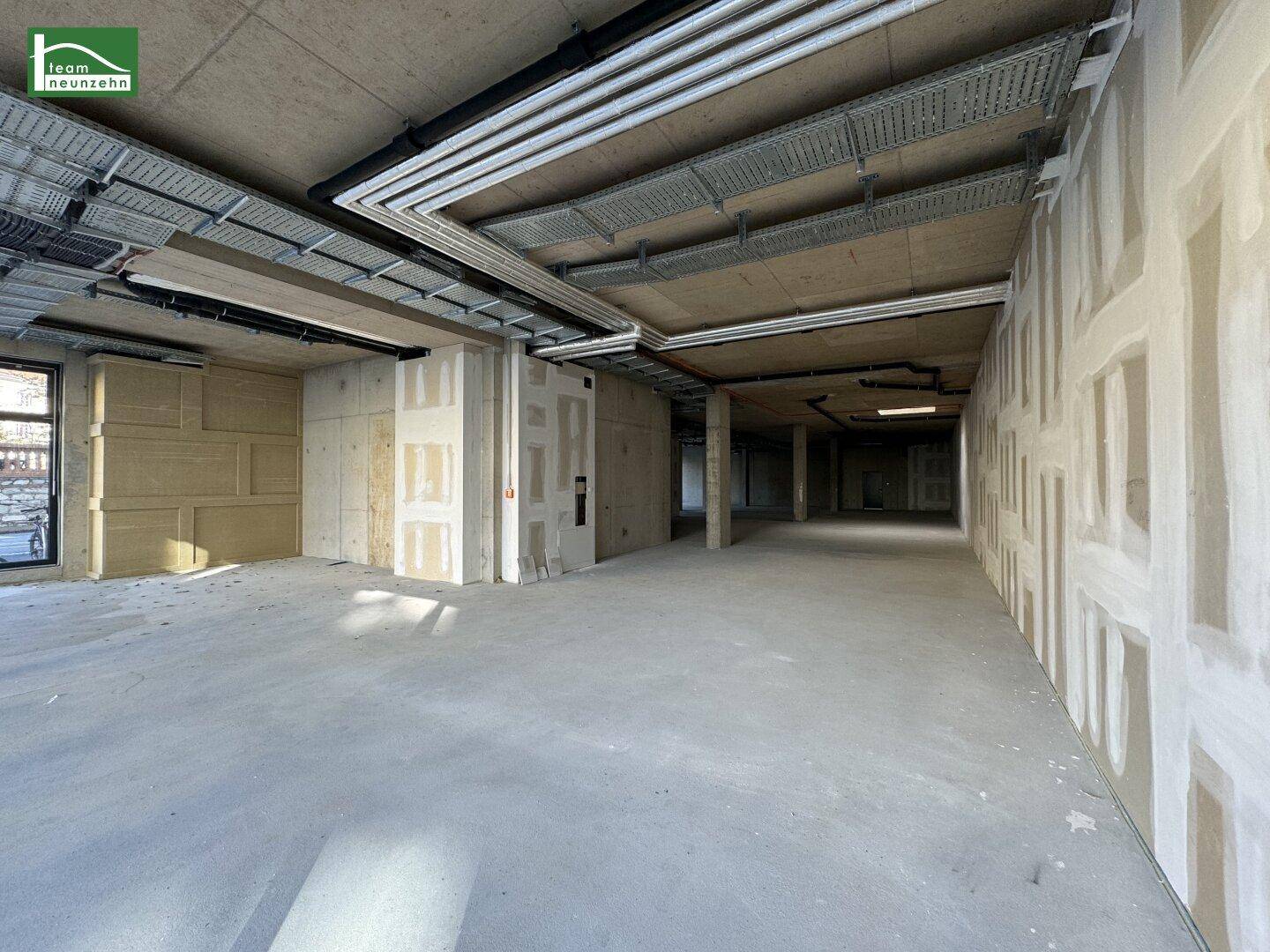 Großer, unfertiger Gewerberaum mit sichtbaren Deckeninstallationen und vorbereiteten Wänden für den Ausbau.