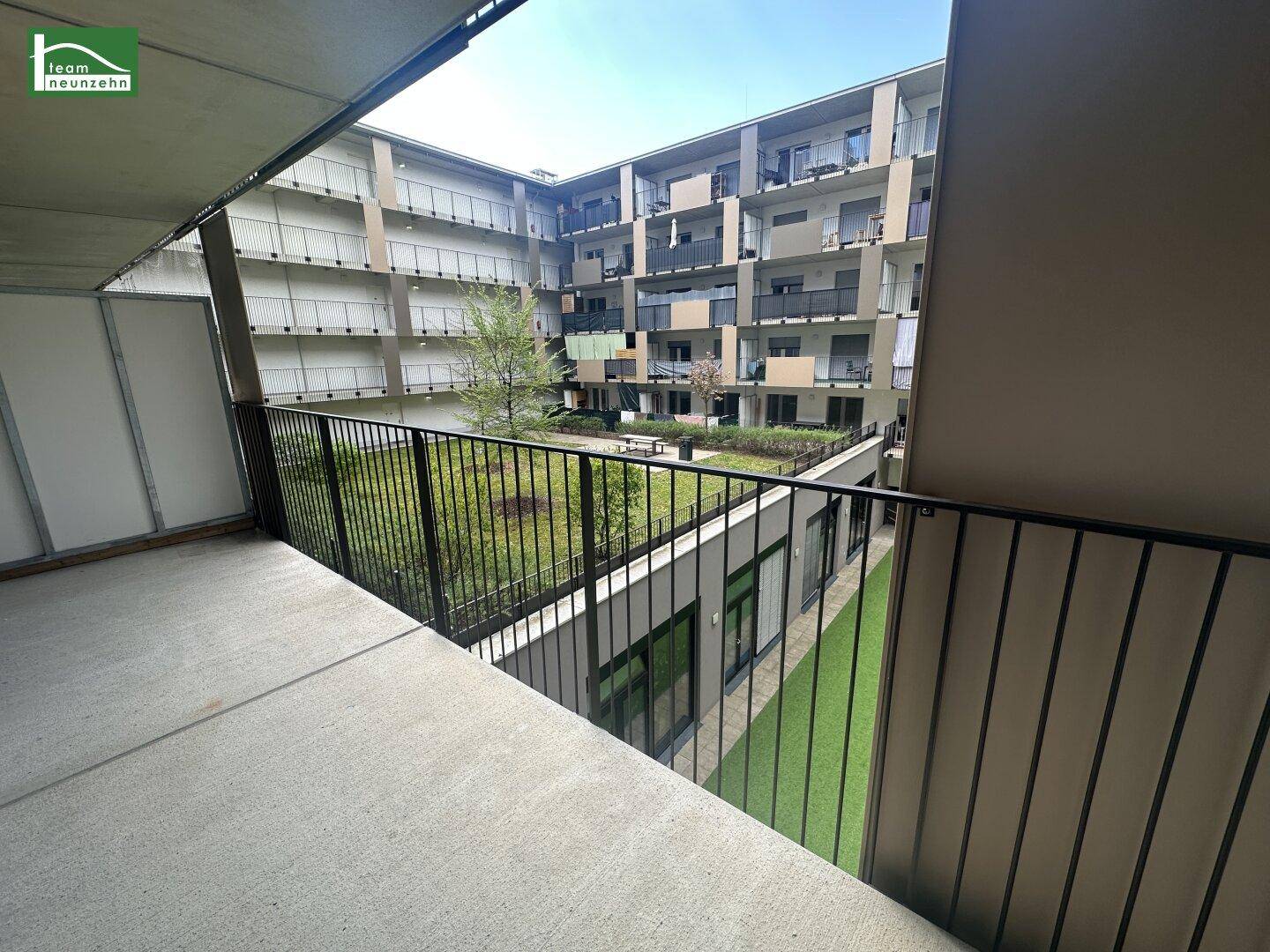Balkon mit Blick auf einen begrünten Innenhof und die umliegenden modernen Gebäude der Anlage.