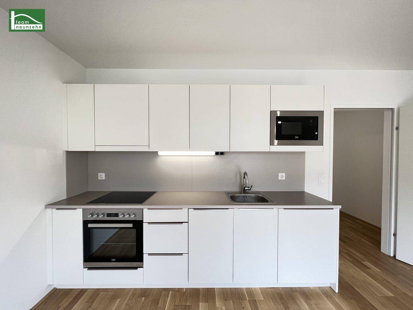 Moderne Küchenzeile mit weißen Schränken, integriertem Backofen und Induktionskochfeld.