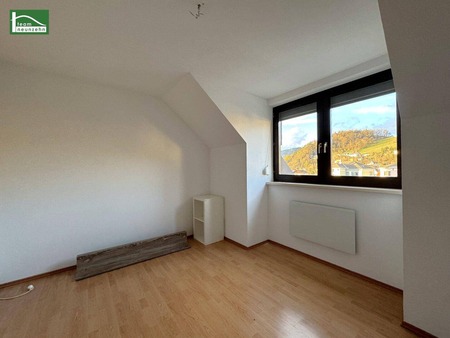 Heller Wohnraum mit Fenster und Blick auf die umliegende Landschaft und Häuser.