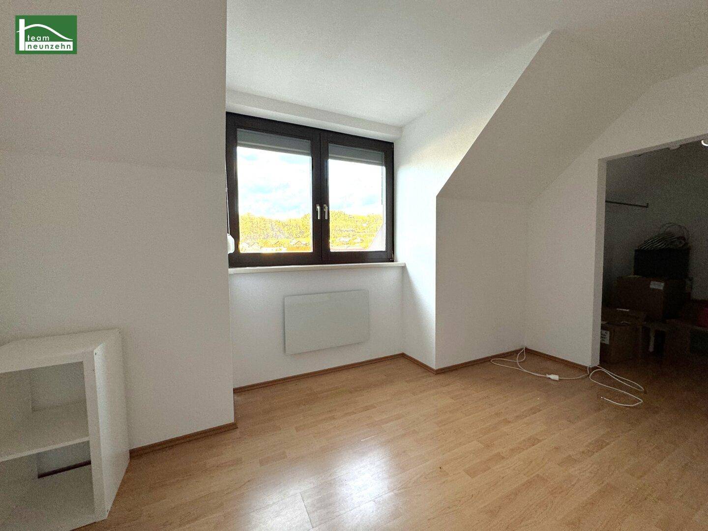 Lichtdurchflutetes Zimmer mit schrägen Wänden und großem Fenster, bietet viel Tageslicht.