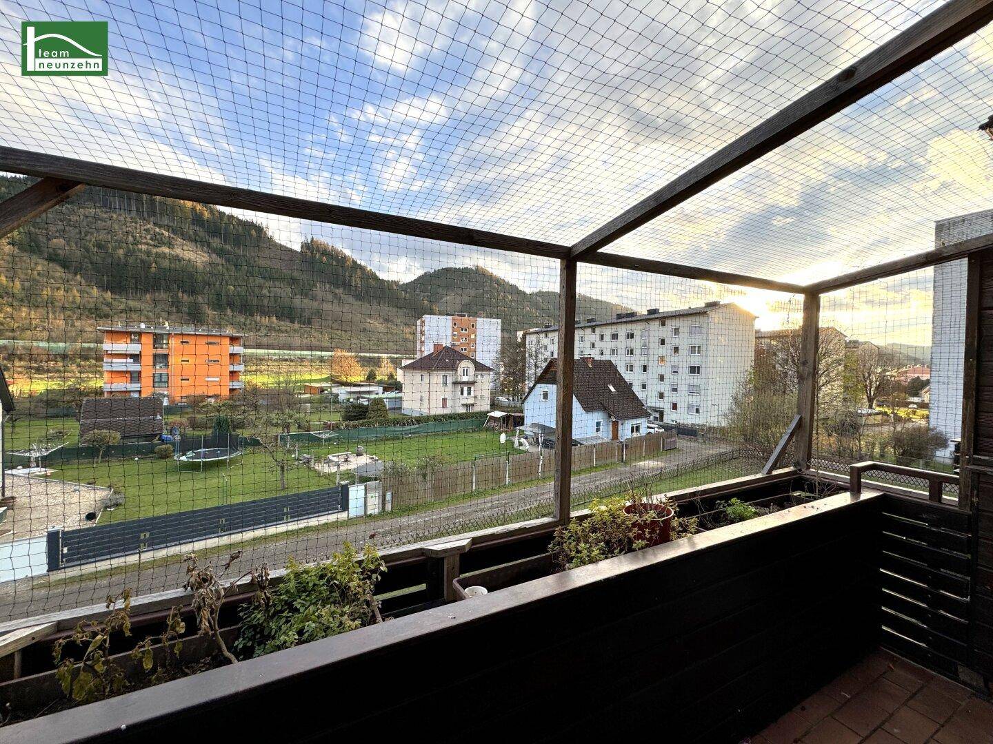 Geräumiger Balkon mit Schutznetz und Panoramablick auf die grüne Umgebung und Gebäude.