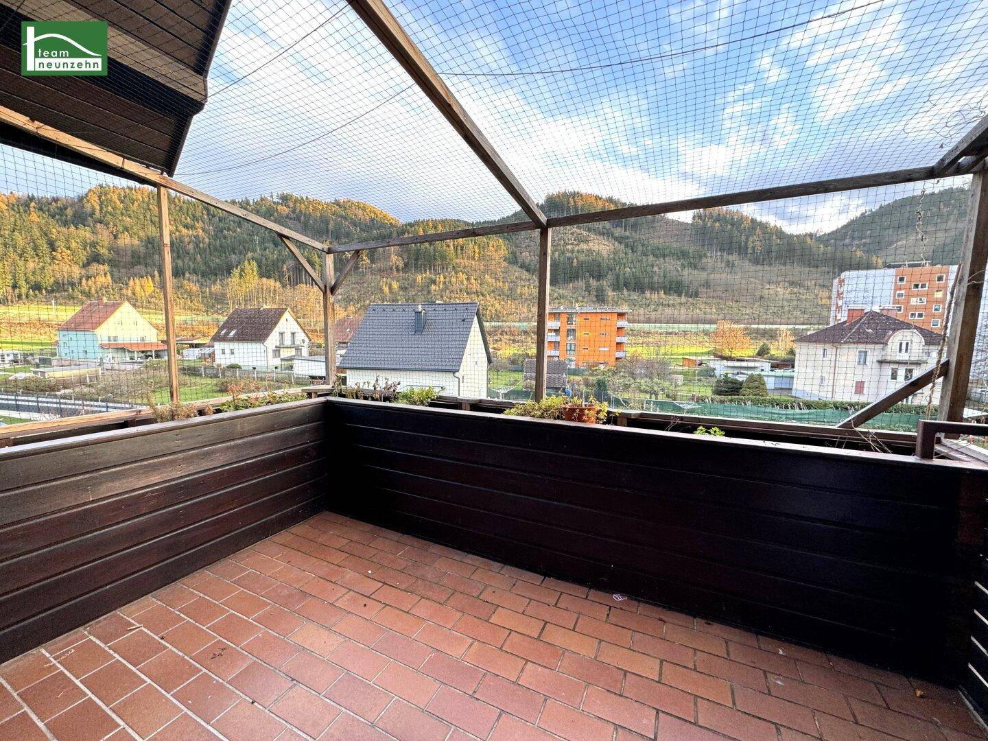 Überdachter Balkon mit Ziegelboden und weitem Blick auf Berge und Wohngebiet.