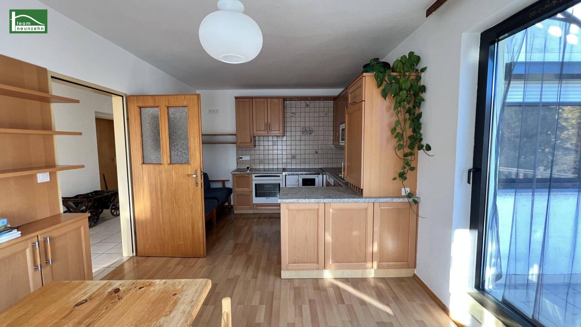 Helle Küche mit Holzschränken, Laminatboden und Zugang zu einem Balkon.