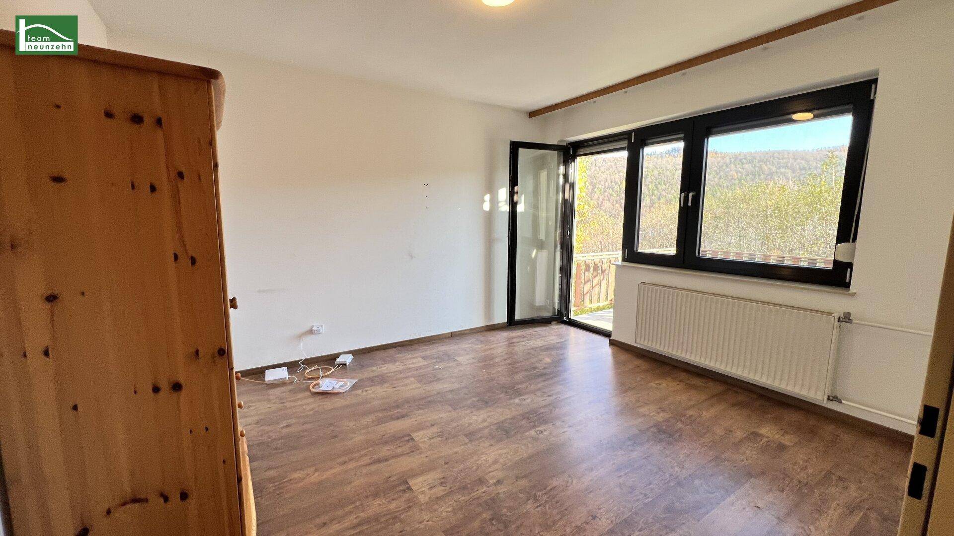 Schlafzimmer mit dunklem Laminatboden und großem Fenster mit Balkonzugang.