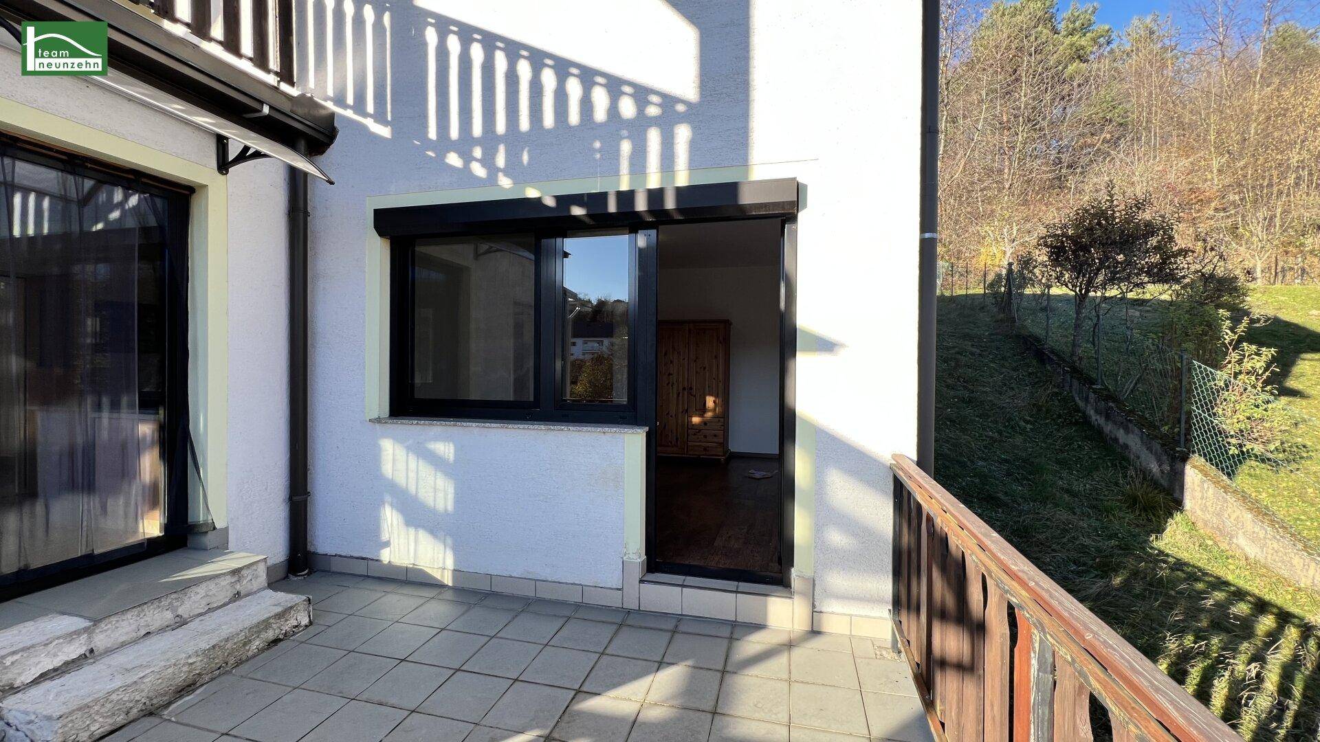 Kleine Terrasse mit Fliesenboden und Zugang zu einem Innenraum, umgeben von Grün.