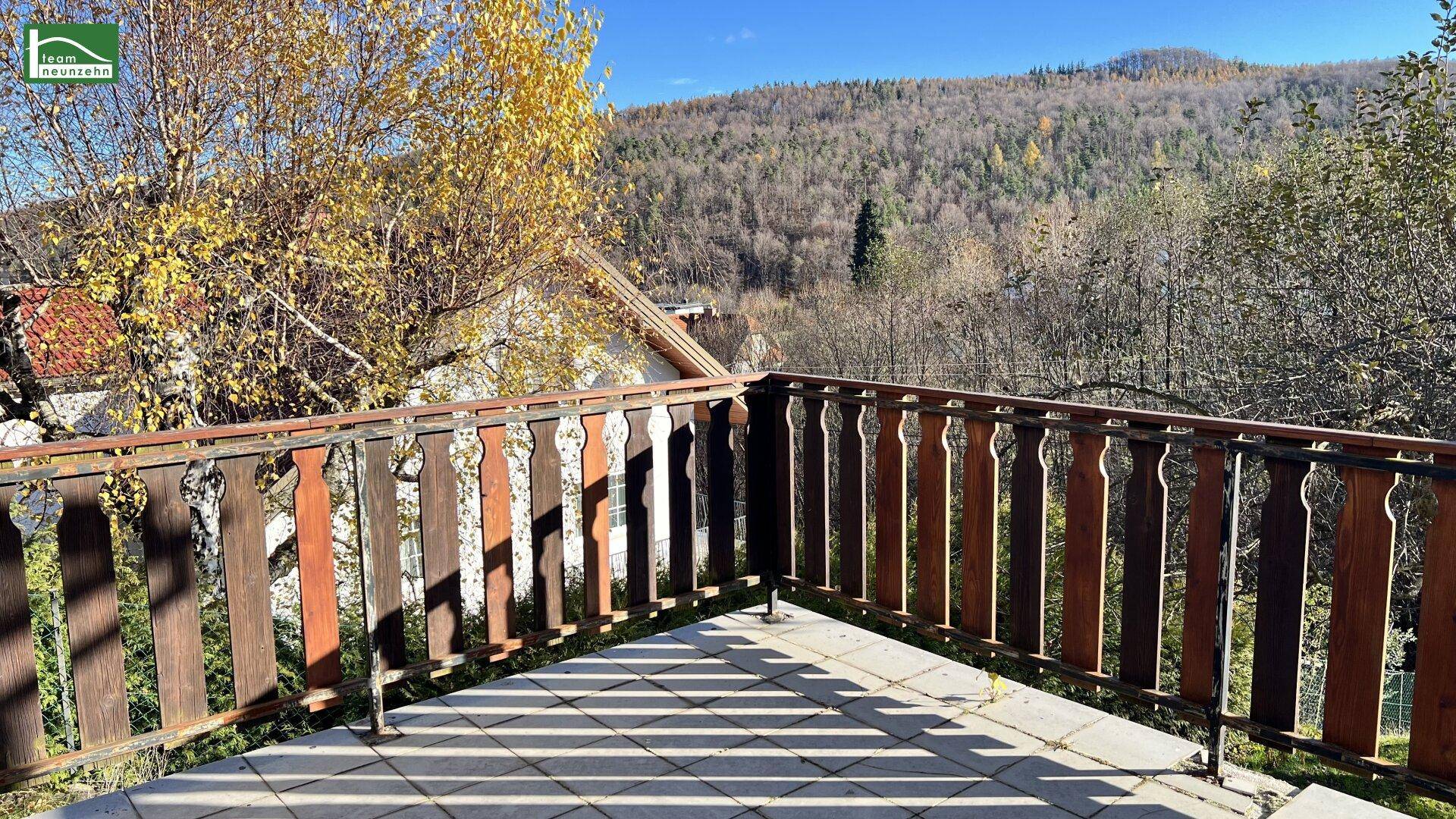 Geräumiger Balkon mit Fliesenboden und Holzgeländer, bietet einen weiten Blick ins Grüne.