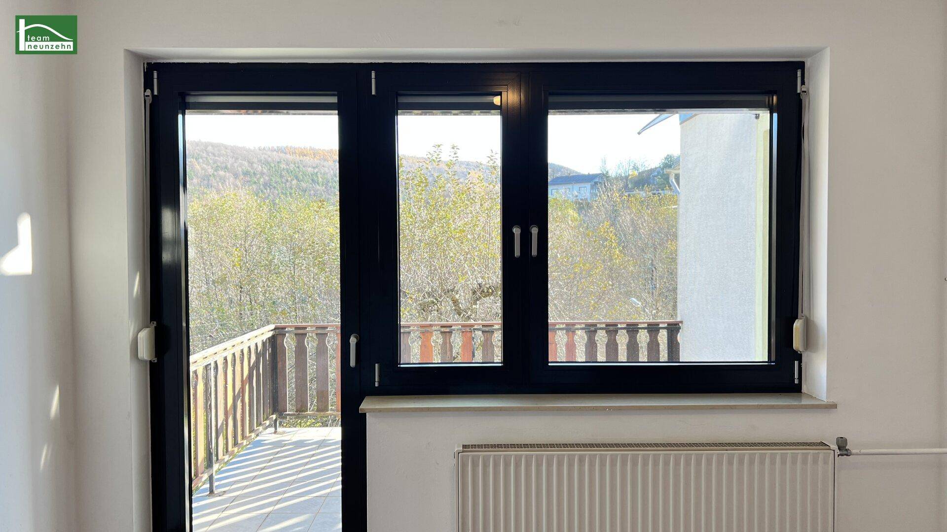 Großes Fenster im Schlafzimmer mit Blick auf die grüne Umgebung und Zugang zum Balkon.