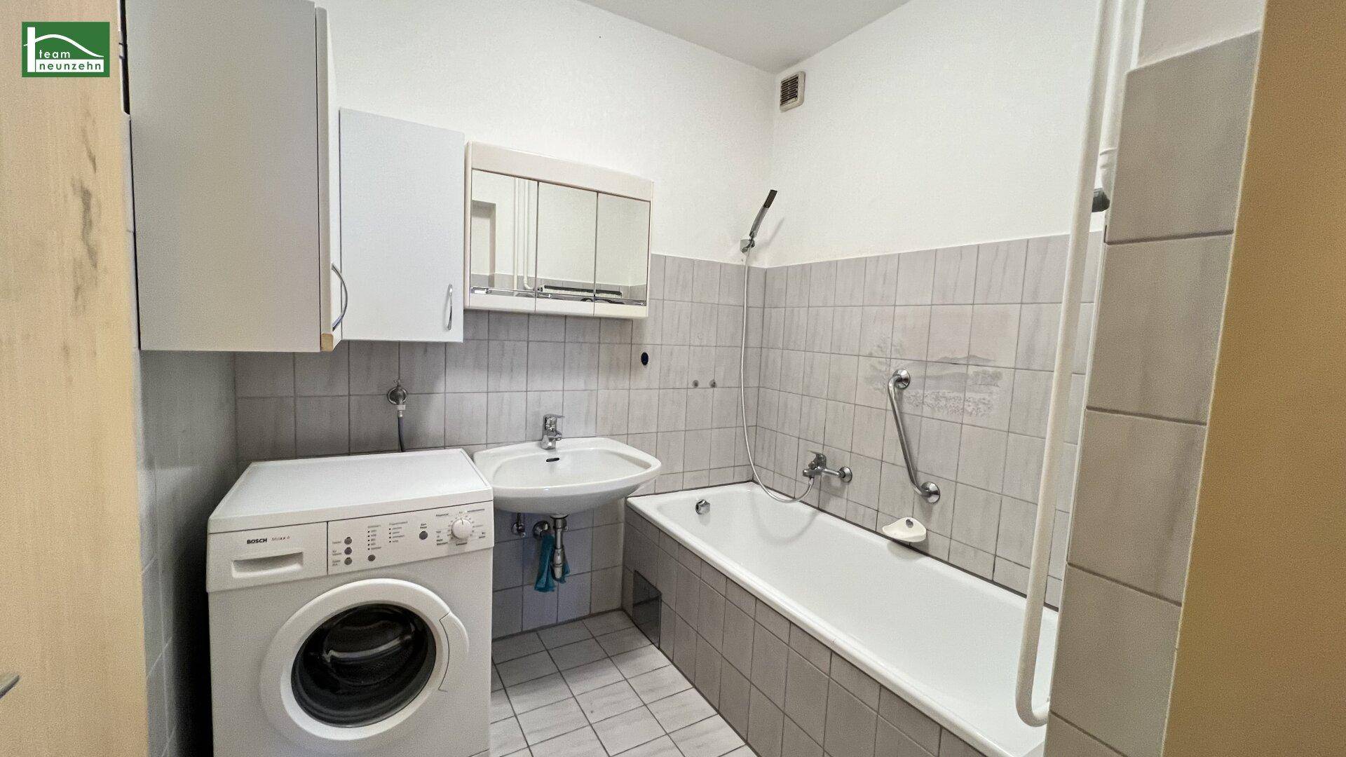 Badezimmer mit Badewanne, Waschbecken und Waschmaschine, hell gefliest.