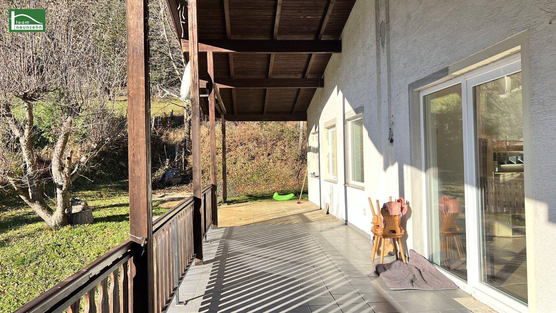 Langer überdachter Balkon mit Holzbalken und Blick auf die grüne Umgebung.