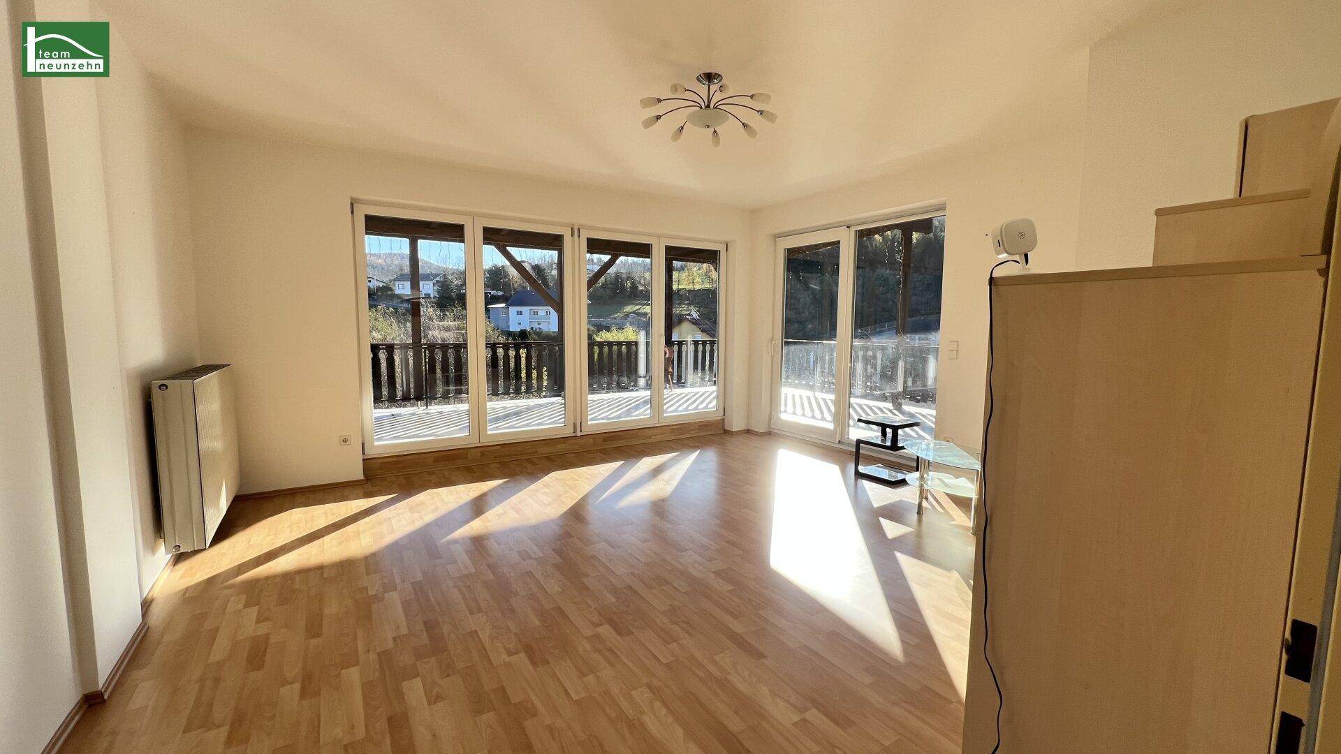 Helles Wohnzimmer mit Parkettboden und Zugang zu einem großen Balkon mit Bergblick.