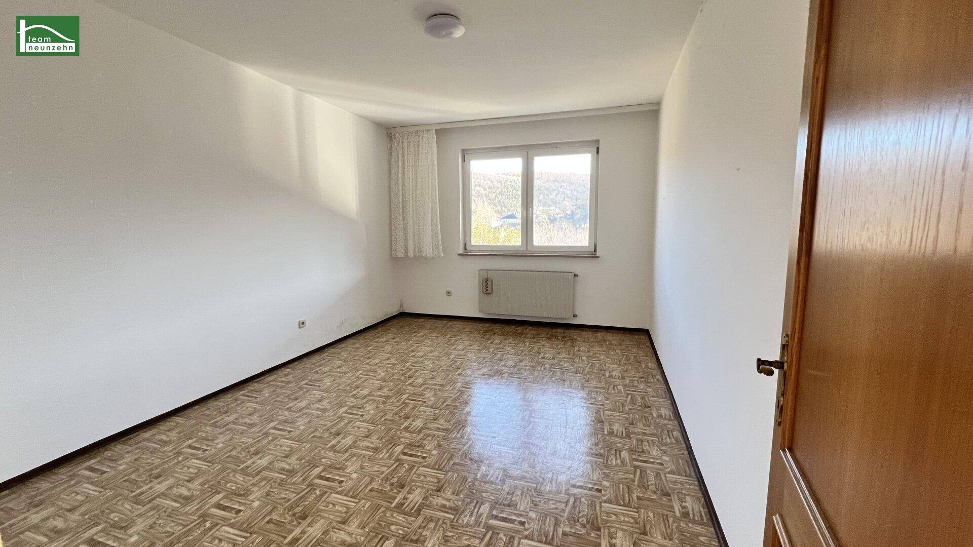 Schlafzimmer mit Parkettboden und Fenster mit Blick ins Grüne, unmöbliert.