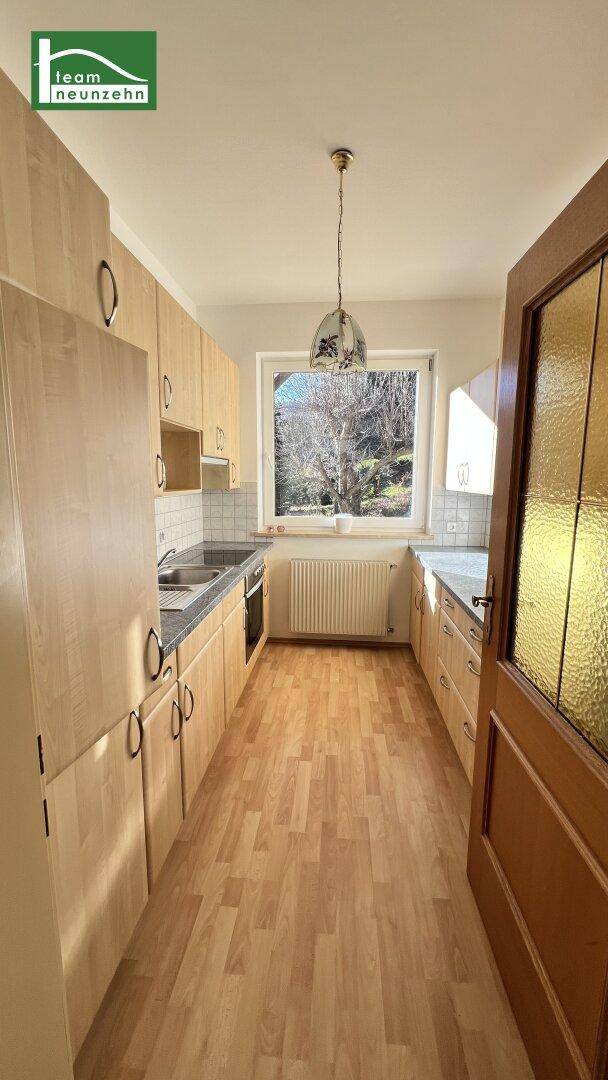 Funktionale Küche mit Holzschränken, Laminatboden und Fenster mit Ausblick.