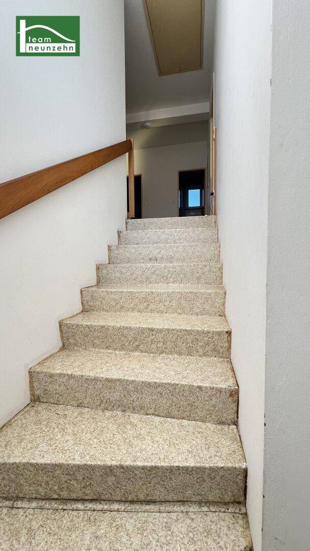 Treppenaufgang mit hellem Terrazzoboden und Holzgeländer, führt in die obere Etage.