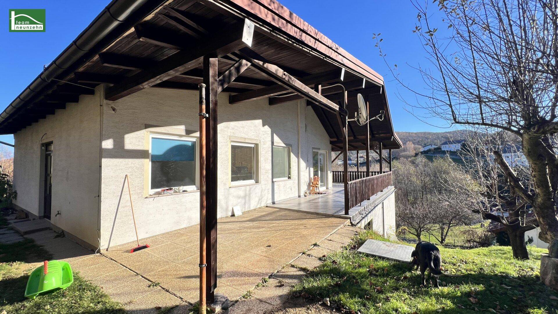Hausfassade mit großer Terrasse und Blick auf die umliegende Landschaft.