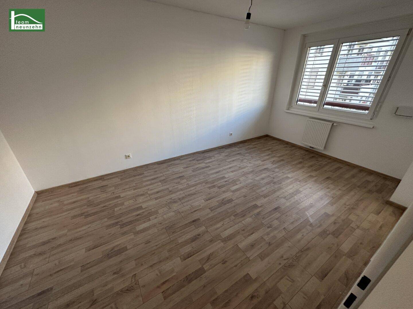 Helles Schlafzimmer mit Holzboden und großem Fenster, bereit zur individuellen Einrichtung.