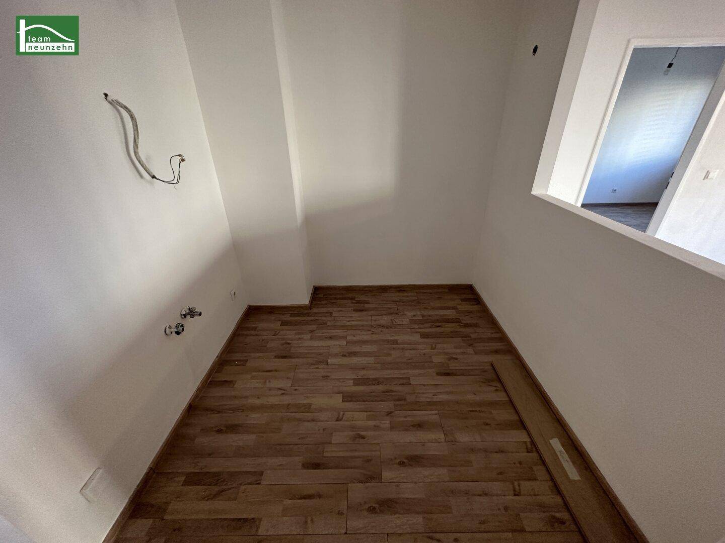 Kleiner Raum mit Holzboden und Anschlüssen für Wasser, ideal als Abstellraum oder Kochnische.
