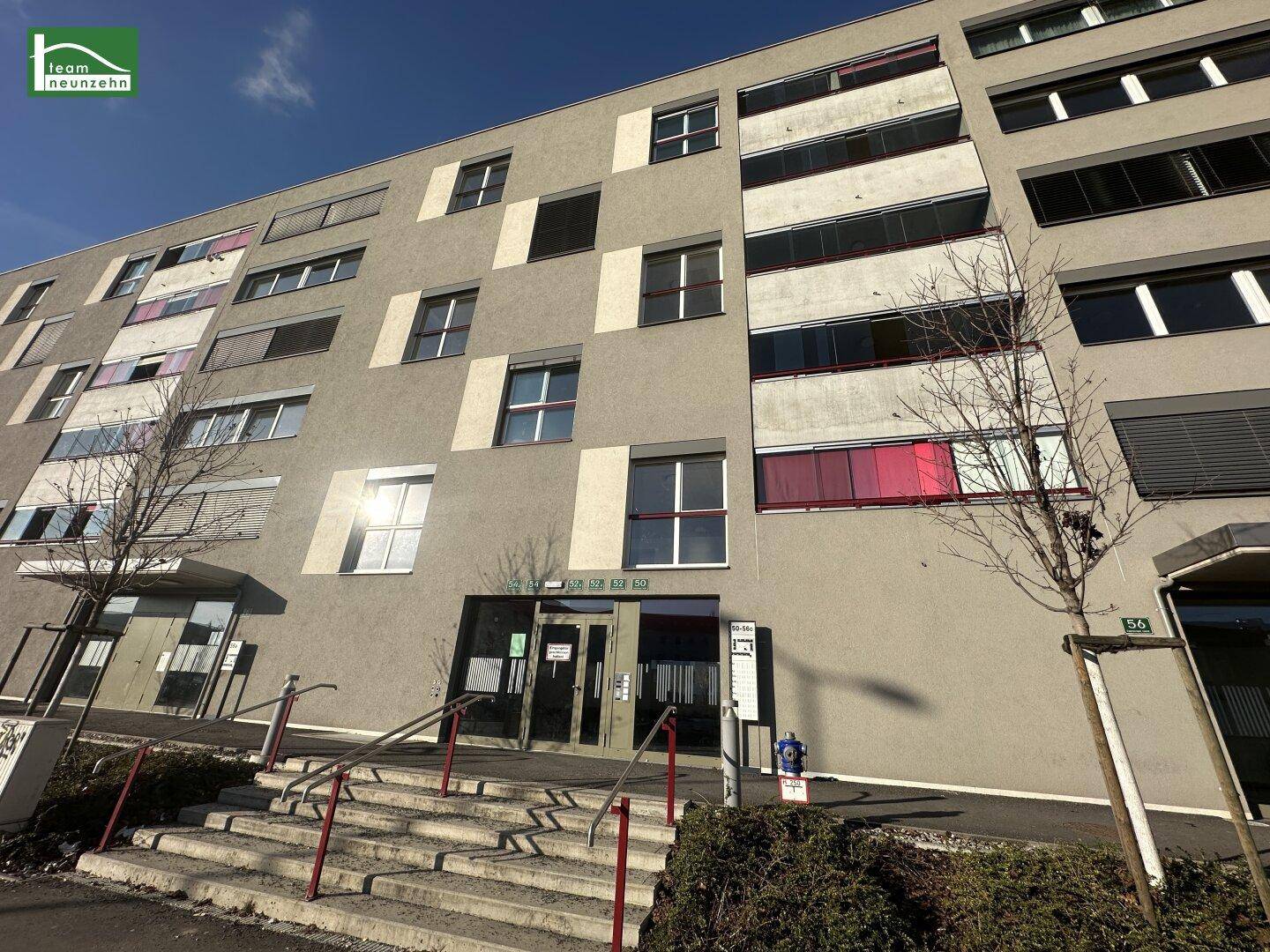 Moderne Fassade eines Mehrfamilienhauses mit verschiedenen Fenstern, Jalousien und einer Rampe am Eingang.
