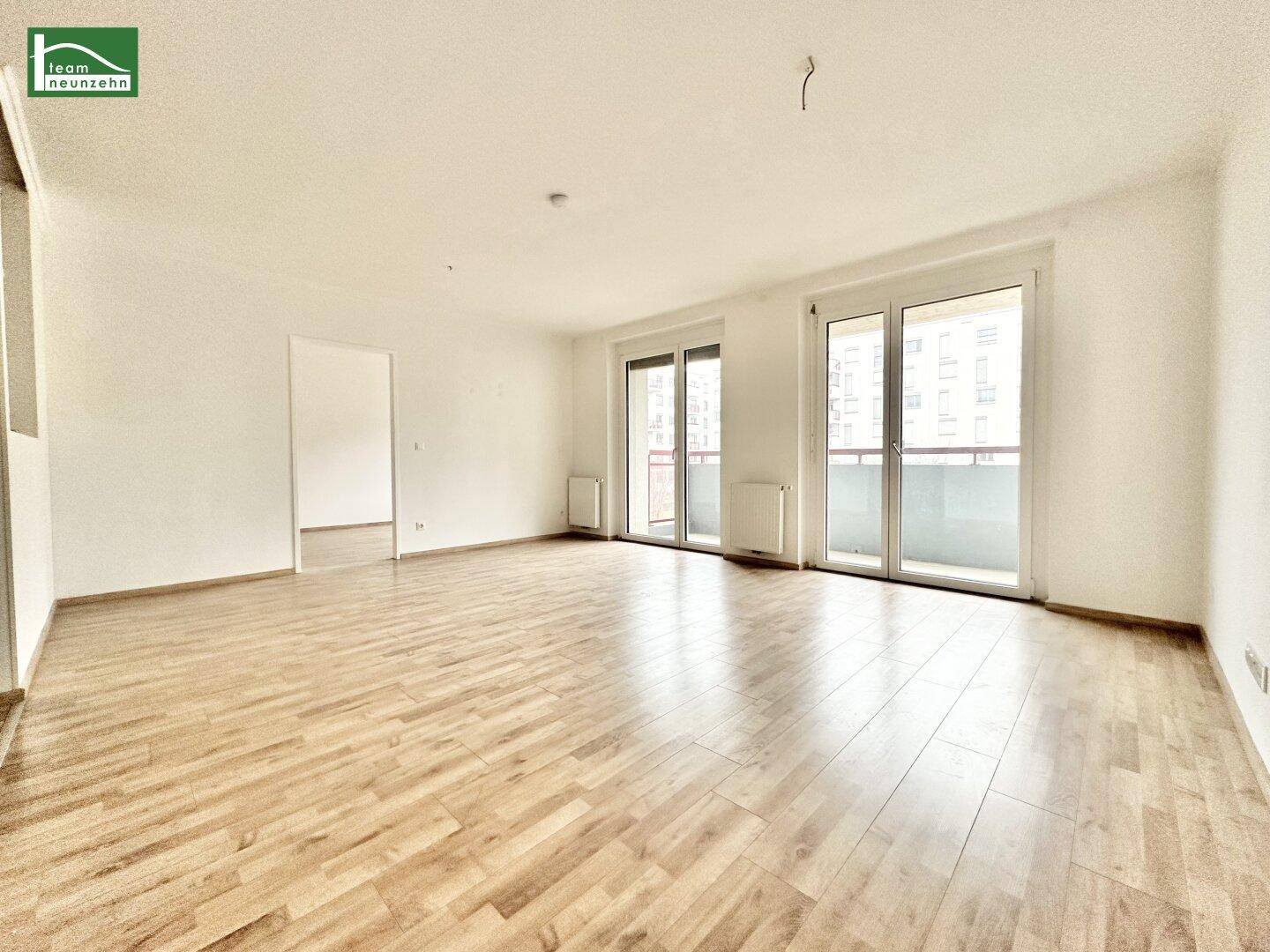 Helles, leeres Wohnzimmer mit Parkettboden und Zugang zu einem Balkon, bereit zum Einzug.