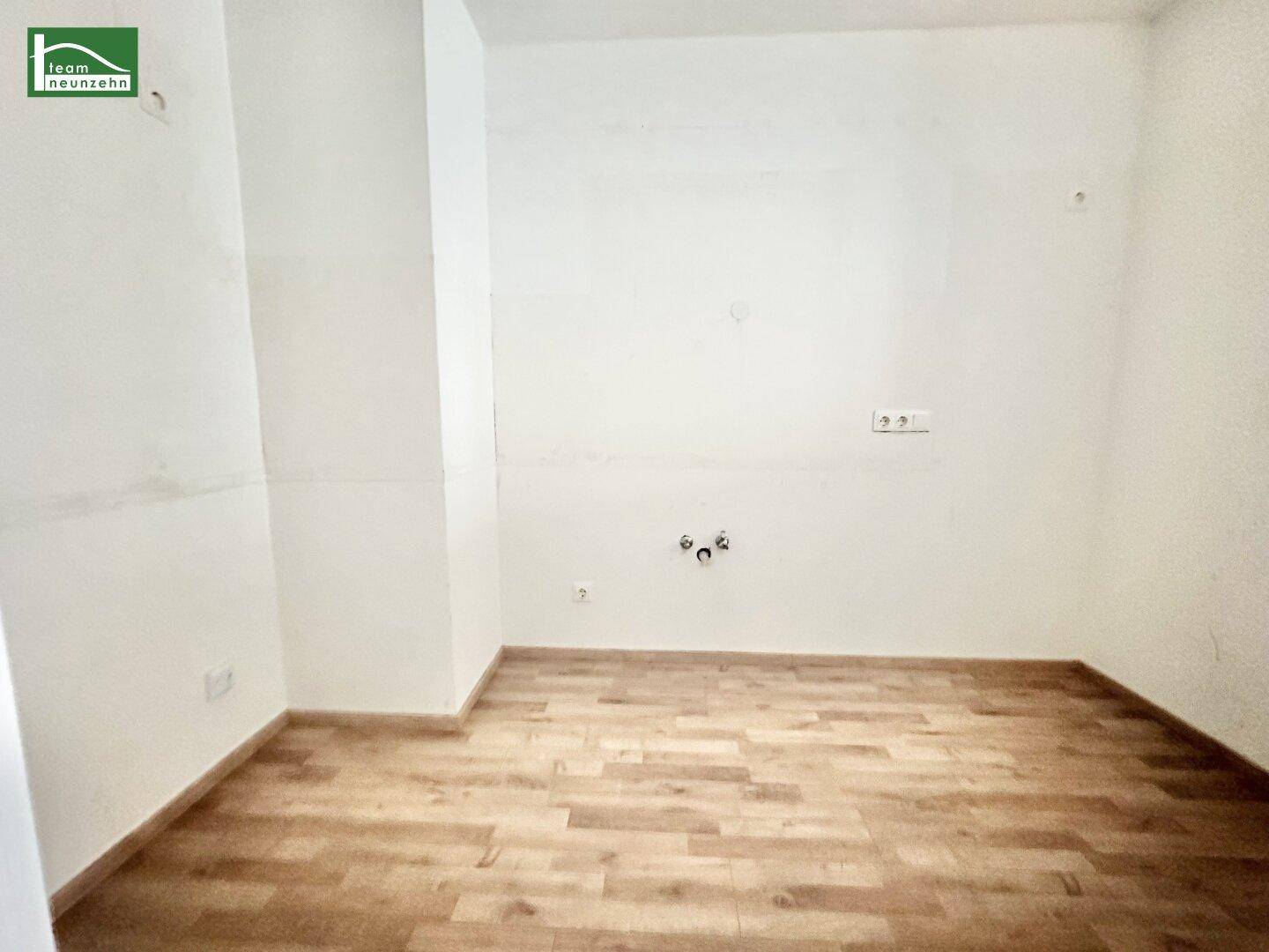 Leerer Raum mit Anschlüssen für eine Küche und Holzboden, bereit für die Installation.