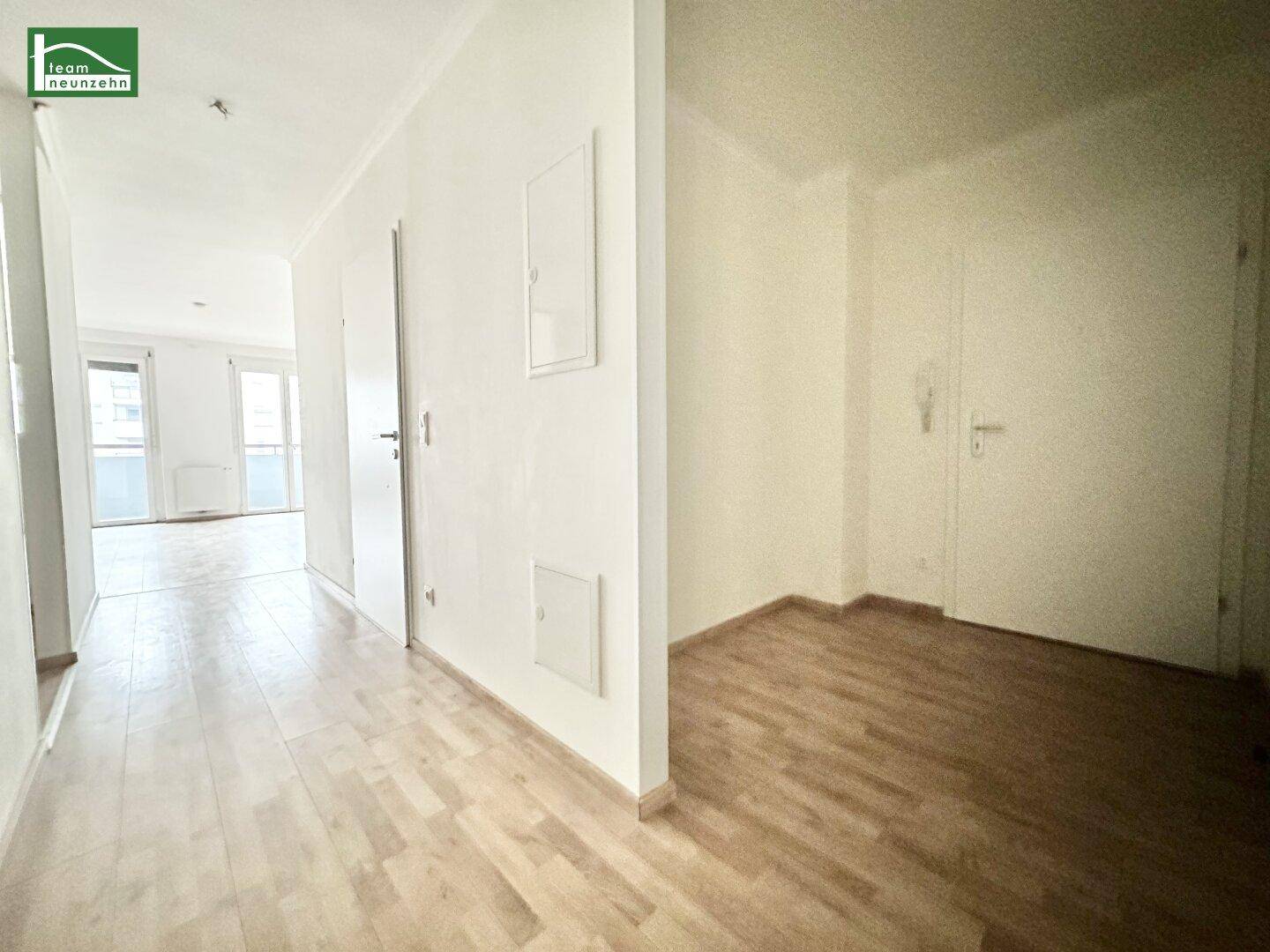 Heller Flur mit Holzboden, der zu verschiedenen Räumen und einem Wohnbereich führt.