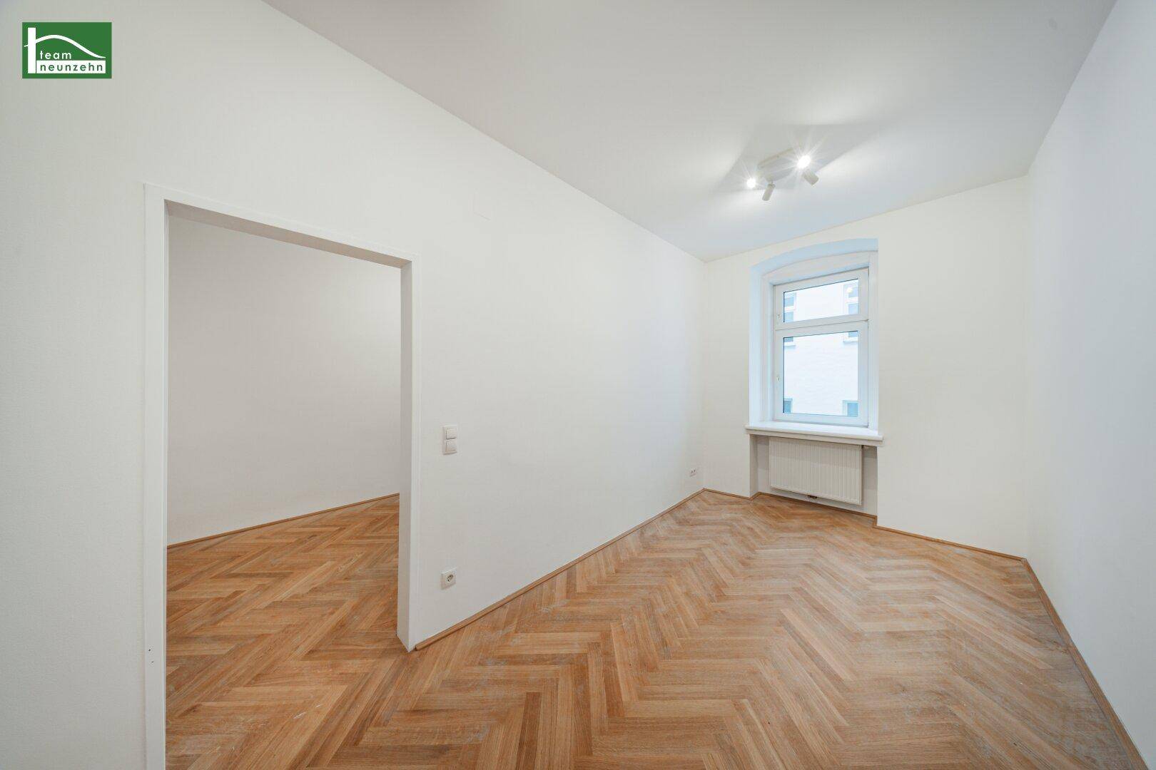 Helles Zimmer mit Fischgrätparkettboden und einem Fenster, das viel Tageslicht hereinlässt.