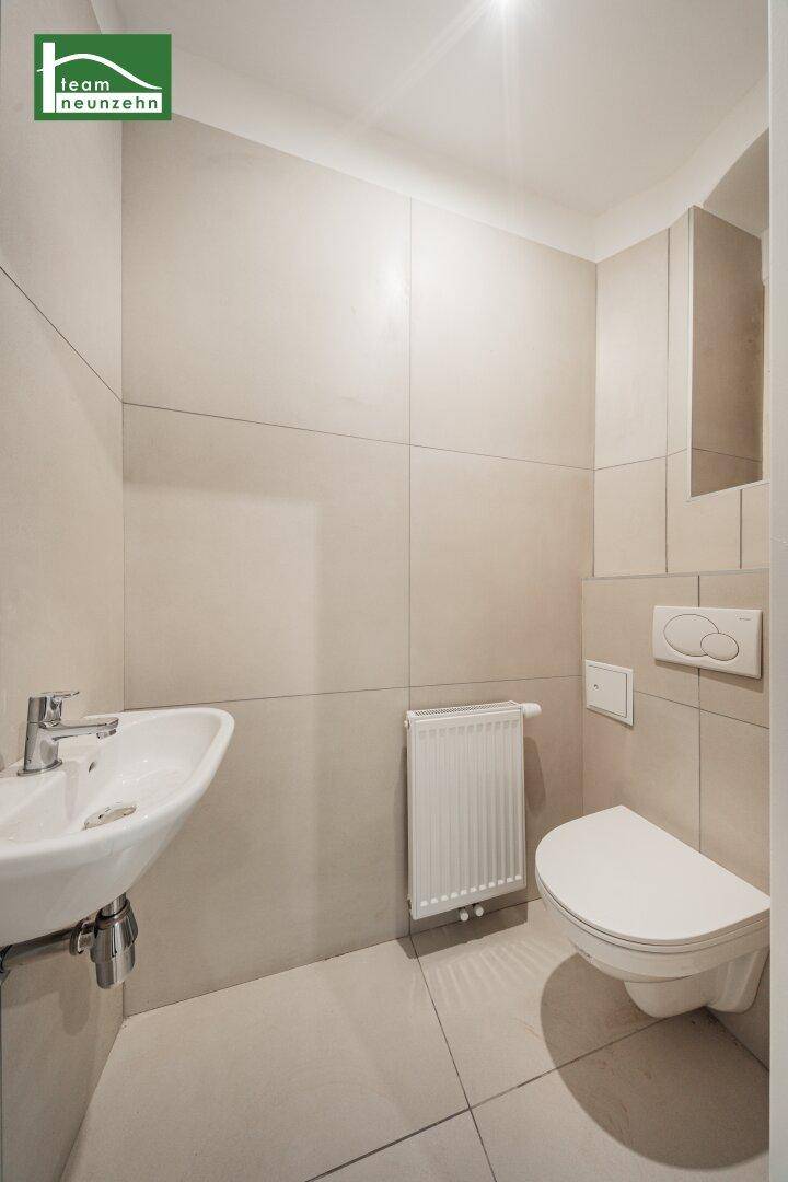 Separates WC mit wandhängender Toilette, kleinem Waschbecken und beigefarbenen Wandfliesen.