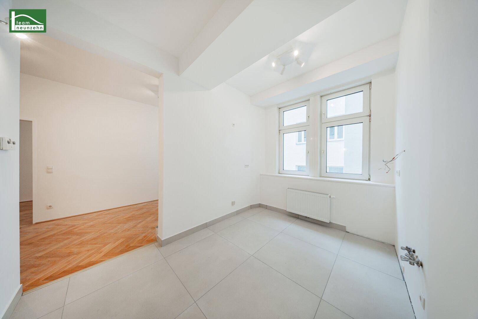Heller Raum mit Fliesenboden und zwei Fenstern, vorbereitet für eine Kücheninstallation.