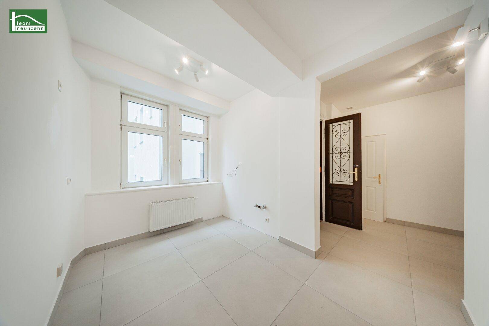 Raum mit Fliesenboden und einem Fenster, das auf einen Innenhof blickt.