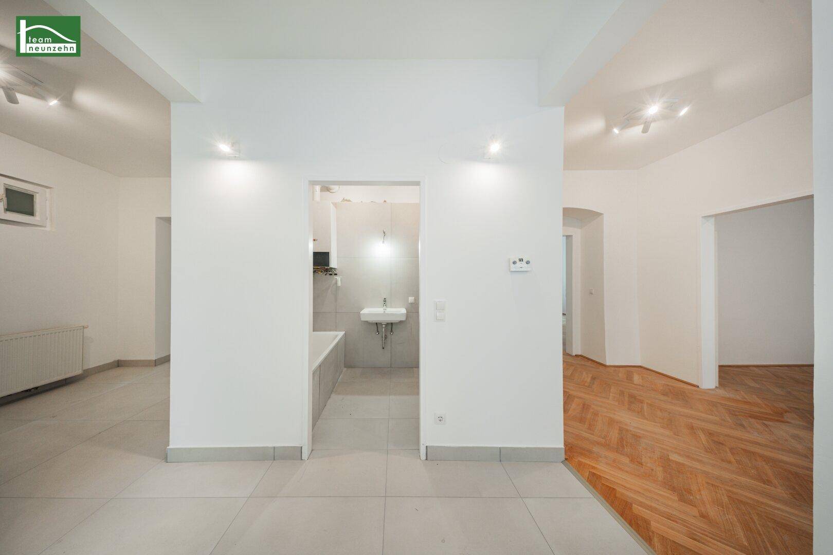 Übergangsbereich mit Fliesenboden und Blick in ein Badezimmer mit Badewanne und Waschbecken.