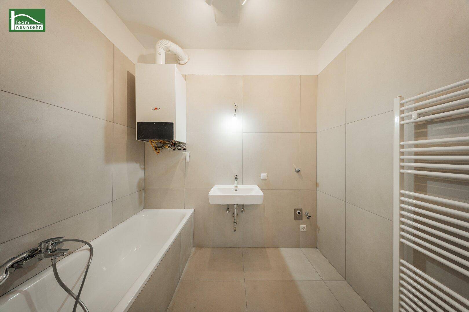 Modernes Badezimmer mit Badewanne, Waschbecken, beigefarbenen Fliesen und einem beheizten Handtuchhalter.