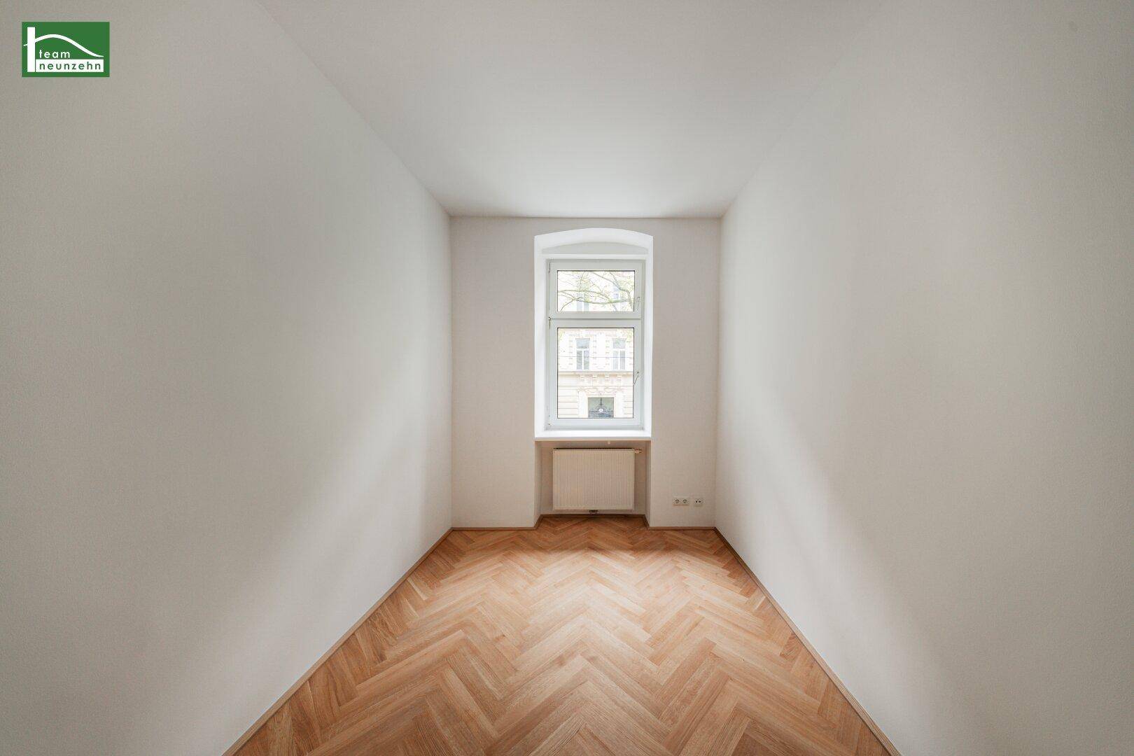 Gemütliches Zimmer mit Fischgrätparkett und einem hohen Fenster, das viel Licht spendet.