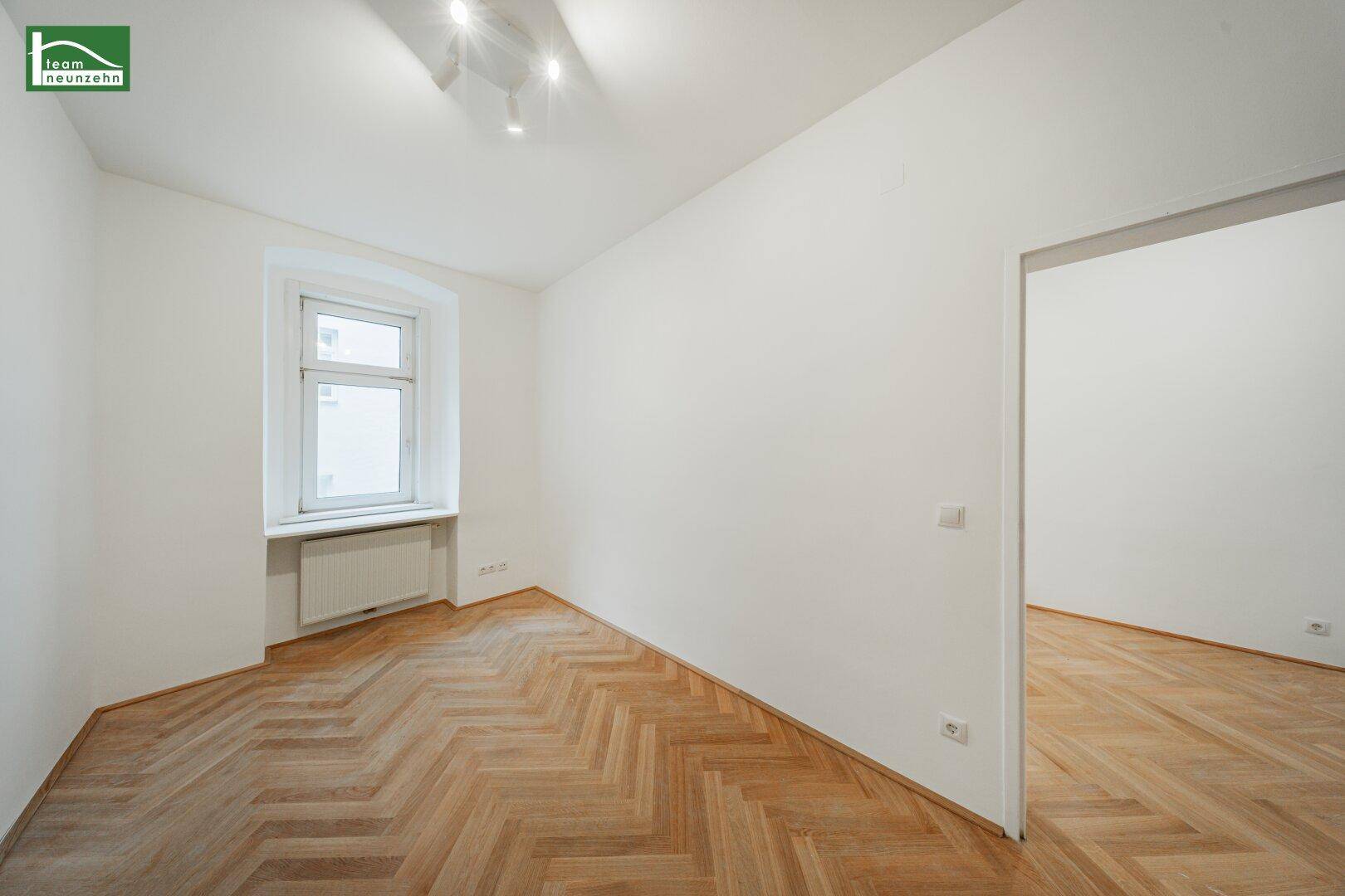 Helles Zimmer mit Fischgrätparkettboden und einem Fenster, das viel Tageslicht hereinlässt.