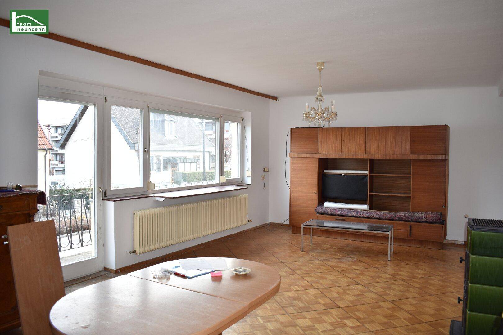 Geräumiges Wohnzimmer mit Parkettboden, großem Fenster und Zugang zum Balkon.