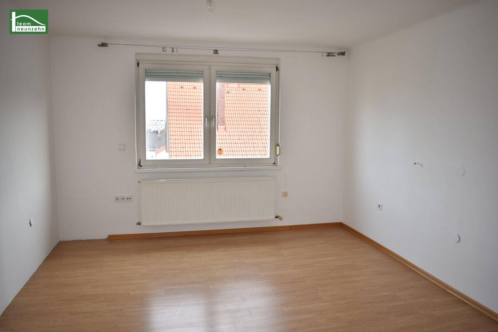 Leeres Schlafzimmer mit Laminatboden, Fenster und Heizkörper unter dem Fenster.